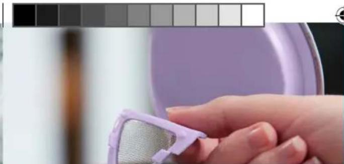 Close-up of a hand holding a purple plastic filter device, with a blurred background showing a dark color swatch (no text or symbols visible)