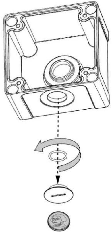 Technical diagram showing a mechanical component with a rotating arrow and a coin for scale, illustrating a mechanical assembly or assembly process.