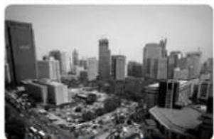 Black-and-white aerial view of a dense urban skyline with high-rise buildings and a prominent low-rise structure (no visible text or signage)