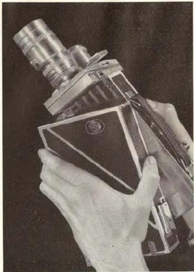 Hand holding a vintage-style optical instrument with a triangular base and lens (no visible text or symbols)