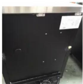 Close-up of a black stainless steel appliance with visible mounting holes and a small label (no readable text or symbols)