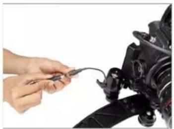 Close-up of hands connecting a cable to a camera lens (no visible text or symbols)