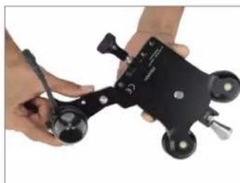 Close-up of hands holding a black mechanical device with four wheels and a pen, no visible text or symbols