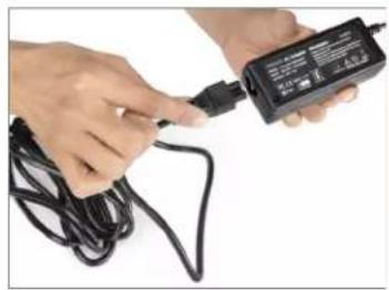 Close-up of hands holding a black electrical charger with coiled cable (no visible text or symbols)