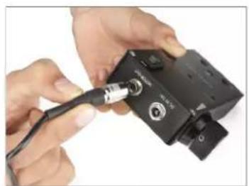 Close-up of hands connecting a black electronic device to a black cable (no visible text or symbols)