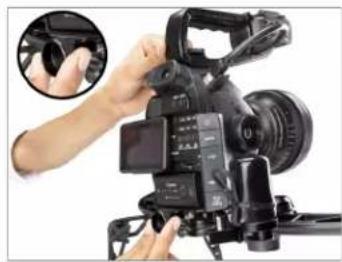 Close-up of a professional video camera with hands adjusting the lens (no visible text or symbols)