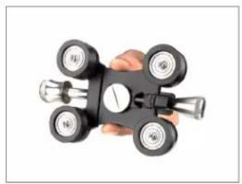 Hand holding a black mechanical device with four wheels and a central dial (no visible text or symbols)