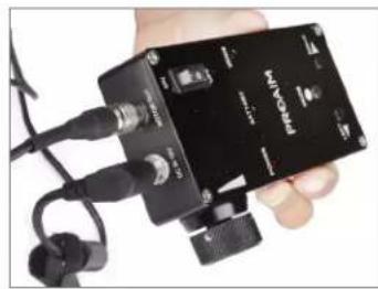 Hand holding a black electronic device with earphones and cables (no visible text or symbols)