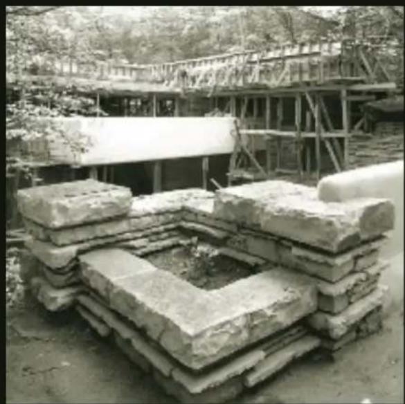 Stacked stone foundation with a central hole, surrounded by trees and scaffolding (no visible text or symbols)