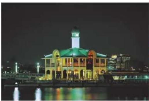 Nighttime exterior view of a historic building with illuminated windows and a central tower, reflected in water (no visible text or signage)
