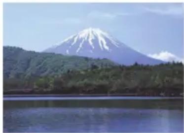 Scenic view of Mount Fuji with snow-capped peaks and green forested hills reflected in calm water.