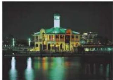 Nighttime exterior view of a historic building with illuminated windows and a central tower, reflected in water (no visible text or signage)