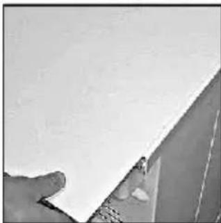 Close-up of a hand holding a white sheet of paper, partially obscured by a wall (no text or symbols visible).
