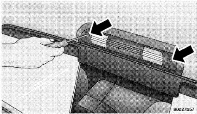 Close-up of a hand using a tool to adjust or install a mechanical component, with arrows indicating the process (no text or symbols visible)