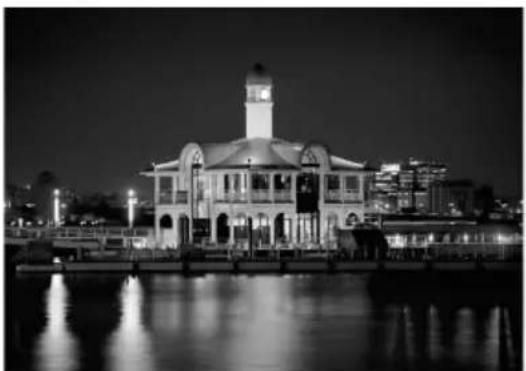 Nighttime exterior view of a historic building with a clock tower and illuminated windows, reflected in calm water, no signage or text visible.