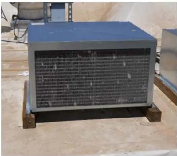 Outdoor photo of a blue industrial enclosure with engraved text panels, placed on wooden pallets.