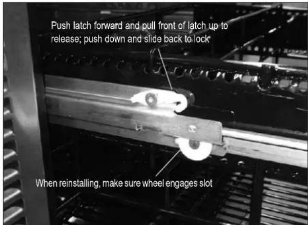 Push latch forward and pull front of latch up to release; push down and slide back to lock When reinstalling, make sure wheel engages slot