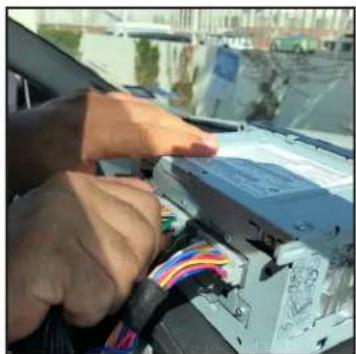 Close-up of hands installing a cable connector into a car's front panel (no visible text or symbols)