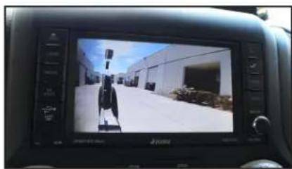 Interior view of a car showing a person on a road with industrial buildings in the background (no visible text or symbols)