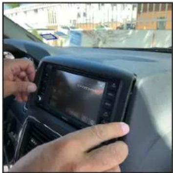 Close-up of a person's hand interacting with a touchscreen display on the car dashboard (no visible text or symbols)