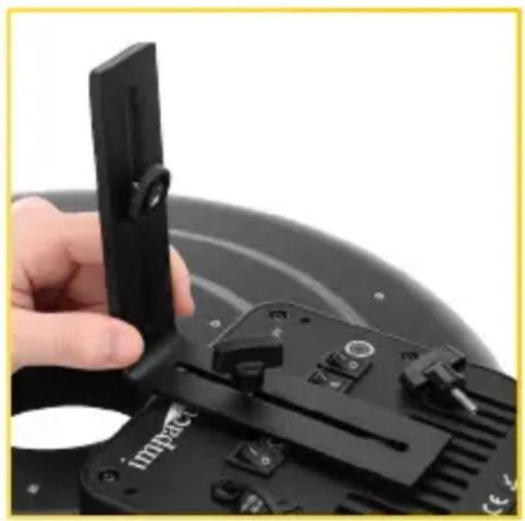 Close-up of a hand holding a black device with a circular button, next to a mechanical component (no visible text or symbols)