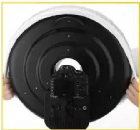 Close-up of hands holding a black circular object with concentric rings, partially obscured by a camera lens (no text or symbols visible)