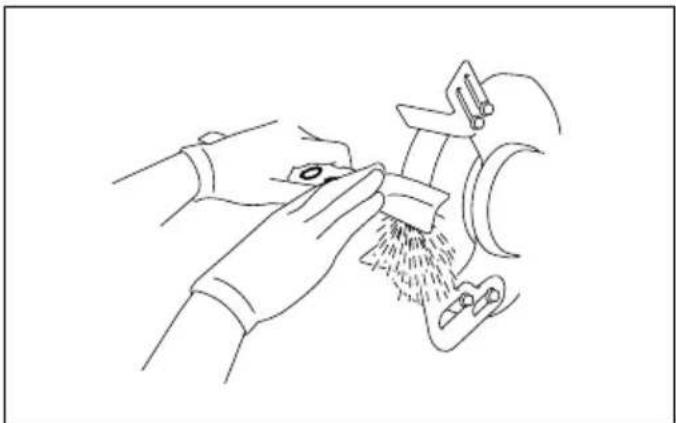 Line drawing of hands using a tool to clean or wash material from a machine (no text or symbols)