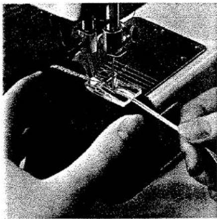 Gros plan de mains manipulant une aiguille de machine à coudre sur un tissu (sans texte ni symboles visibles)