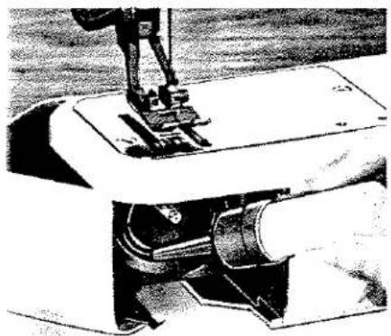 Gros plan d'une aiguille de machine à coudre piquant un tuyau cylindrique (sans texte ni symboles visibles)