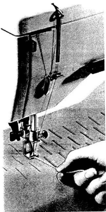 Gros plan sur l'aiguille d'une machine à coudre piquant un tissu, avec une main tenant la lame (aucun texte ou symbole visible).
