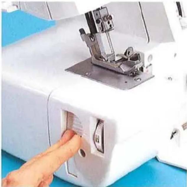 Gros plan sur une aiguille de machine à coudre insérée dans une fente, avec une main ajustant le composant (aucun texte ou symbole visible)