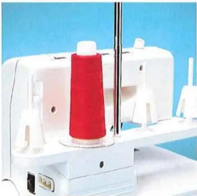 Gros plan d'une machine à coudre avec une bobine de fil rouge et une base blanche, sur fond bleu (aucun texte ou symbole visible).