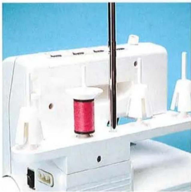 Gros plan d'une machine à coudre blanche avec bobine et aiguille, sur un fond bleu (aucun texte ou symbole visible)