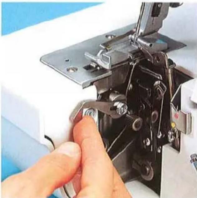Gros plan d'une main actionnant l'aiguille d'une machine à coudre, montrant les composants métalliques et les boutons de réglage (aucun texte ou symbole visible)