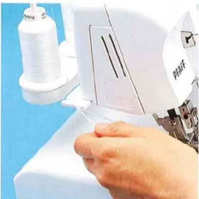 Gros plan d'une main actionnant une machine à coudre avec une bobine et un équipement industriel à proximité (aucun texte ou symbole visible).