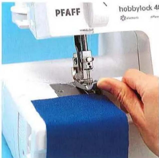 Gros plan d'une main actionnant une machine à coudre PFAFF avec du tissu bleu, aucun texte ou symbole visible sur la machine elle-même.