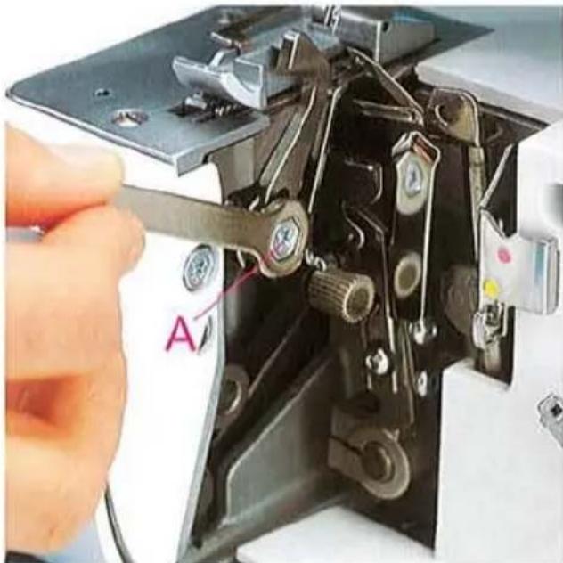 Gros plan de l'aiguille d'une machine à coudre en cours de réglage, montrant des pinces métalliques et des boutons de réglage (aucun texte ou symbole visible)