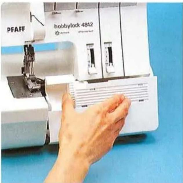Main actionnant une machine à coudre PFAFF avec un fond bleu (aucun texte ou symbole visible sur la machine elle-même)