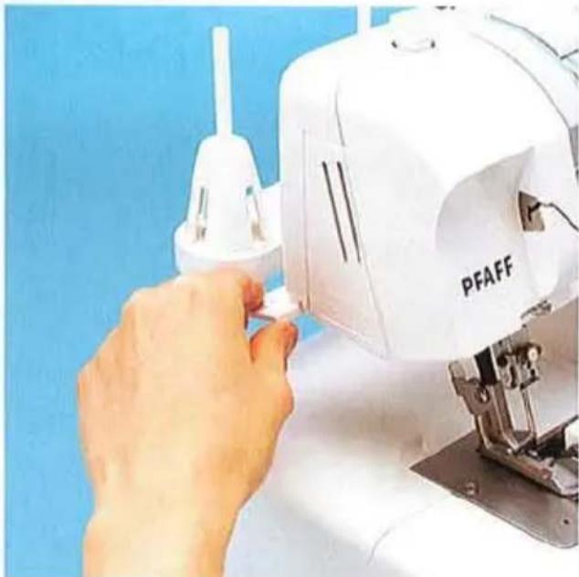 Gros plan d'une main utilisant une machine à coudre PFAFF sur fond bleu (aucun texte ou symbole visible sur le corps de la machine).