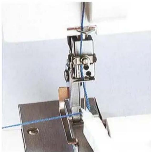 Gros plan d'une aiguille de machine à coudre cousant du tissu, avec une main gantée visible (aucun texte ni symbole).