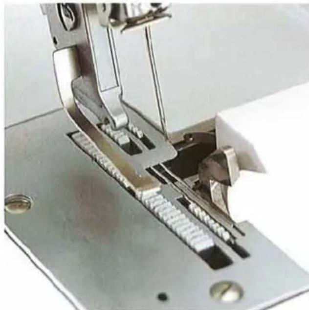 Gros plan d'une aiguille de machine à coudre cousant une tôle (aucun texte ni symbole visible).