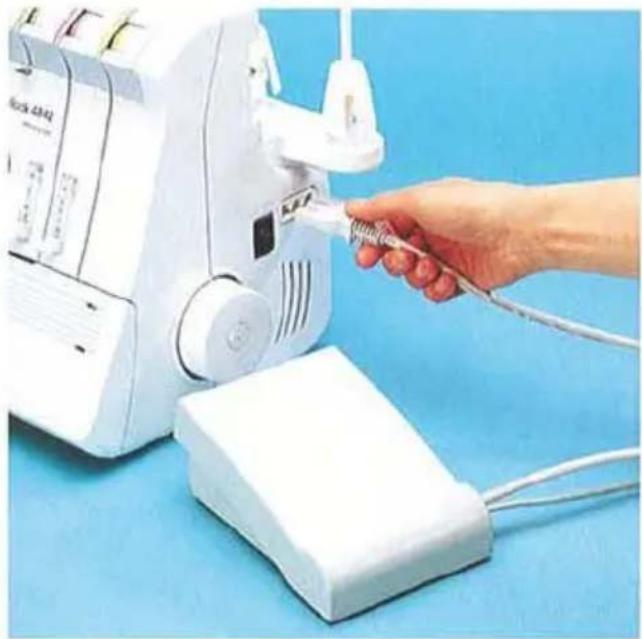 Main insérant un câble dans une machine à coudre blanche sur un fond bleu (aucun texte ou symbole visible)