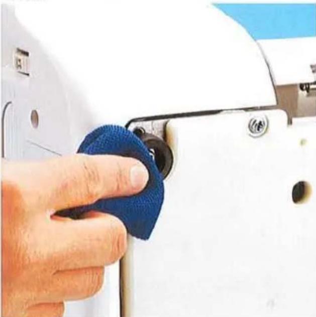Gros plan d'une main nettoyant une machine à coudre blanche avec un chiffon bleu (aucun texte ou symbole visible)
