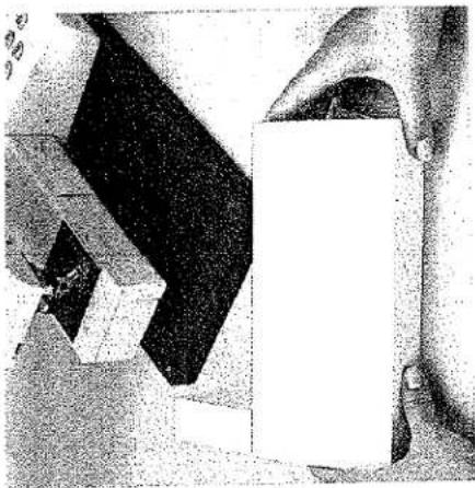 Gros plan sur des mains manipulant un objet rectangulaire blanc avec un bloc noir en forme de L au-dessus (aucun texte ou symbole visible)