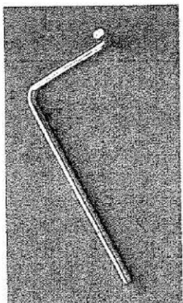 Gros plan d'une tige métallique avec une pointe et une petite extrémité circulaire, posée sur une surface texturée (aucun texte ni symbole visible)