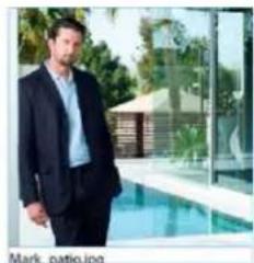 Man in business suit standing by a pool with glass building and trees in background (no visible text or symbols)