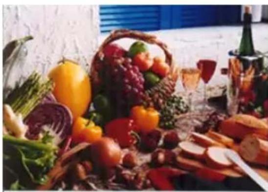 Assorted fresh vegetables and snacks including a basket, fruits, and wine bottle on a table (no visible text or labels)
