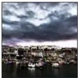 Black-and-white photo of a coastal town with boats on calm water under a cloudy sky (no visible text or symbols)