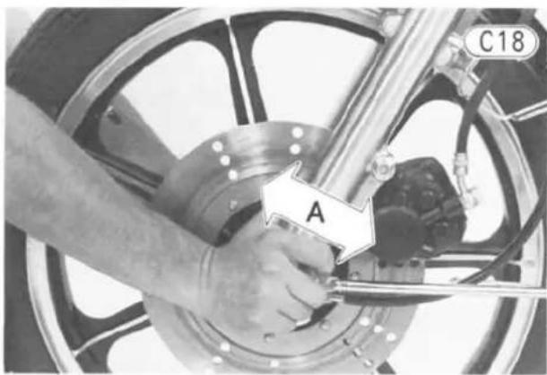 Close-up of a person adjusting a bicycle wheel with a tool, labeled 'A' and 'C18' (no readable text beyond labels)