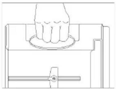 Line drawing of a hand pressing down on a circular component within a mechanical housing (no text or symbols)